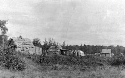 Black-and-white historic photo of small wooden buildings in a rural settlement near trees.