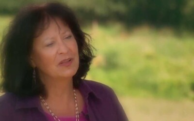 Person in a purple shirt sits outdoors against a soft green background.