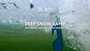 Title card for The Ways episode "Deep Snow Camp: Ice Fishing and Subsistence Harvest," photographed from beneath the ice looking up through a freshly drilled hole. An ice chisel penetrates the surface from above, surrounded by shattered ice and churning bubbles, with green lake water visible below. Text is rendered in white bold type with small orange and blue diamond decorative elements.