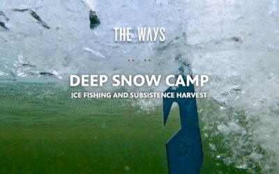 Title card for The Ways episode "Deep Snow Camp: Ice Fishing and Subsistence Harvest," photographed from beneath the ice looking up through a freshly drilled hole. An ice chisel penetrates the surface from above, surrounded by shattered ice and churning bubbles, with green lake water visible below. Text is rendered in white bold type with small orange and blue diamond decorative elements.
